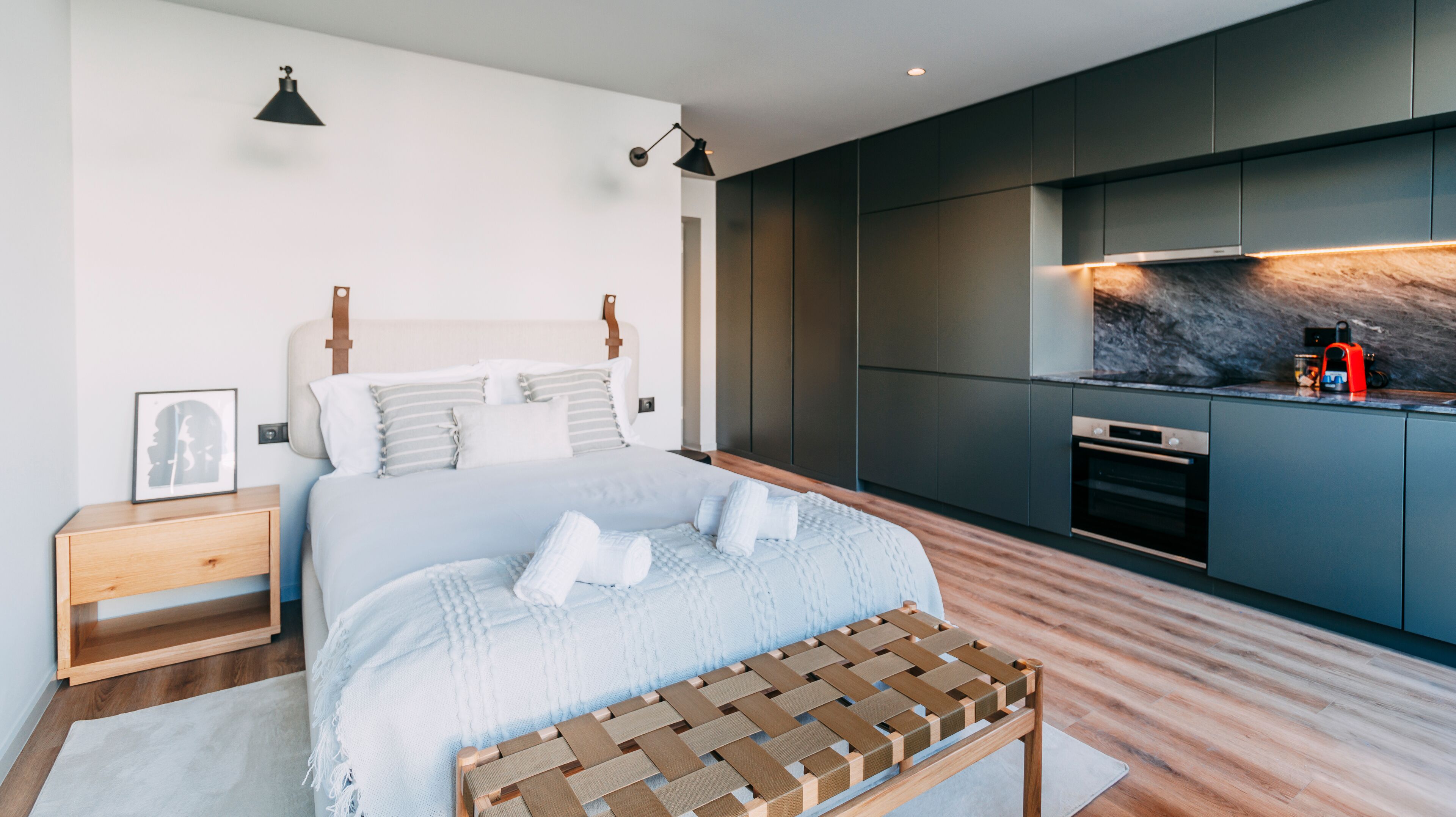 Una camera da letto moderna con un letto grande, comodini, una panca, un angolo cottura con mobili scuri e una schiena di marmo.