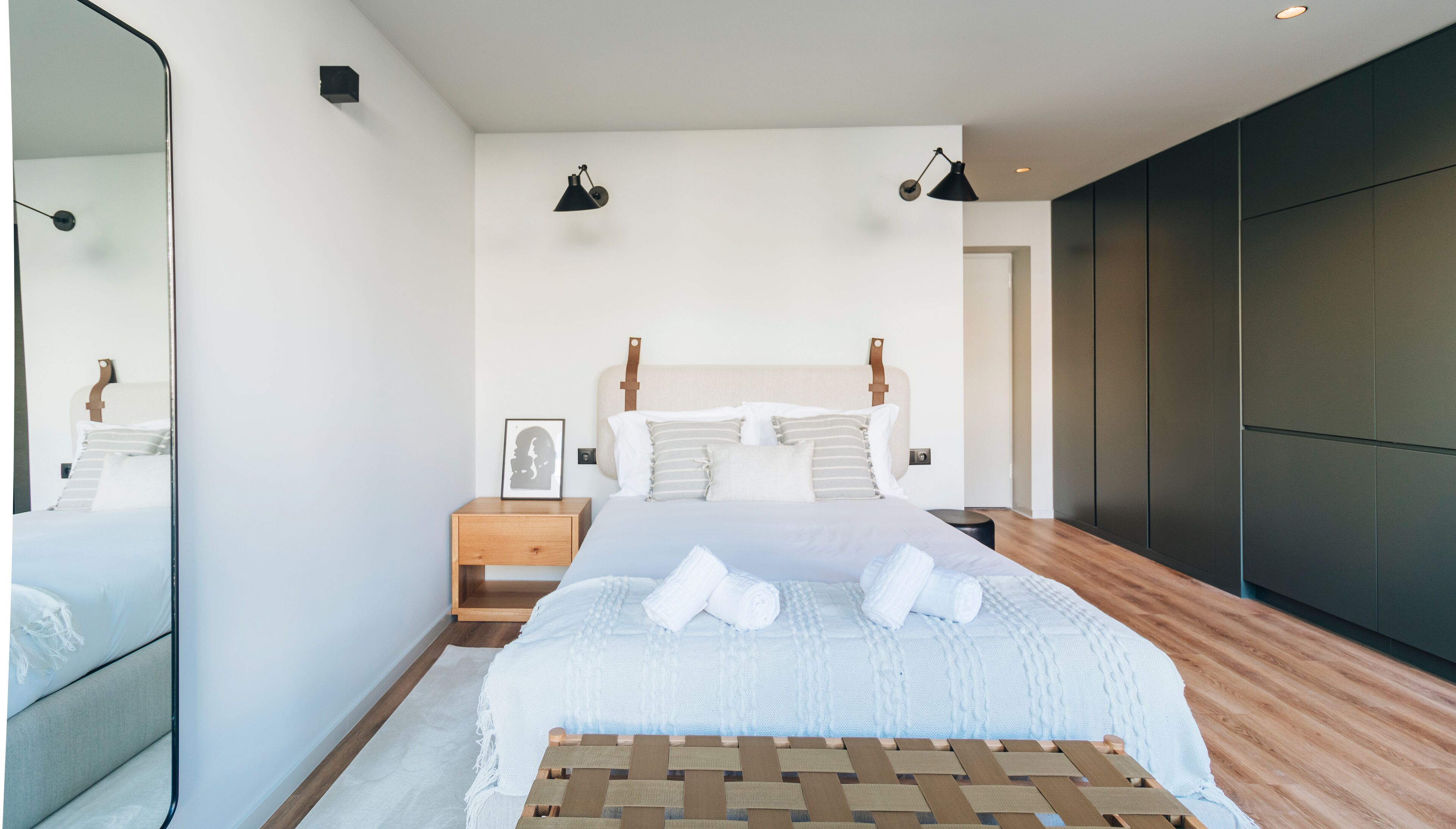 A modern bedroom with a large bed, bedside lamps, a nightstand, and a framed picture on the wall.