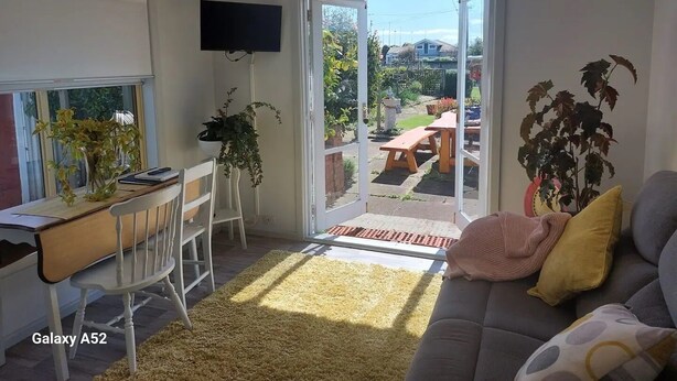 A modern living room with a Galaxy A52 smartphone on a desk, a sofa, and a dining area with a table and chairs.