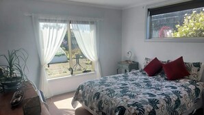 A bedroom with a bed, a bedside table, a window with curtains, and a view of the outdoors.