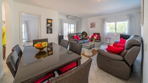 A modern living room with a glass-top dining table, comfortable seating, and a large window providing natural light. - Sharon: Semi-detached house with sea views and private pool (L'Escala)