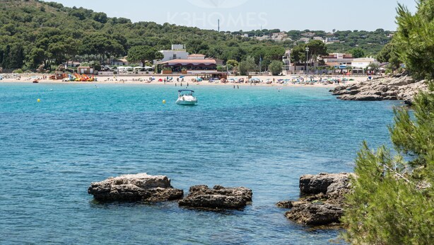 A coastal beach scene with clear blue water, rocky outcrops, and buildings in the background. - Sharon: Semi-detached house with sea views and private pool (L'Escala)