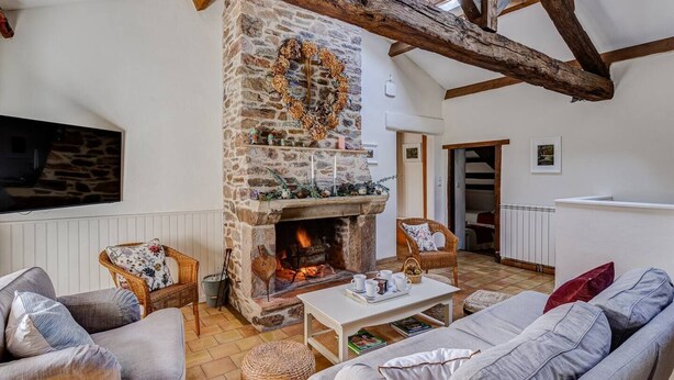 Ein gemütliches Wohnzimmer mit Kamin aus Stein, Holzbalken und bequemen Sitzmöglichkeiten.