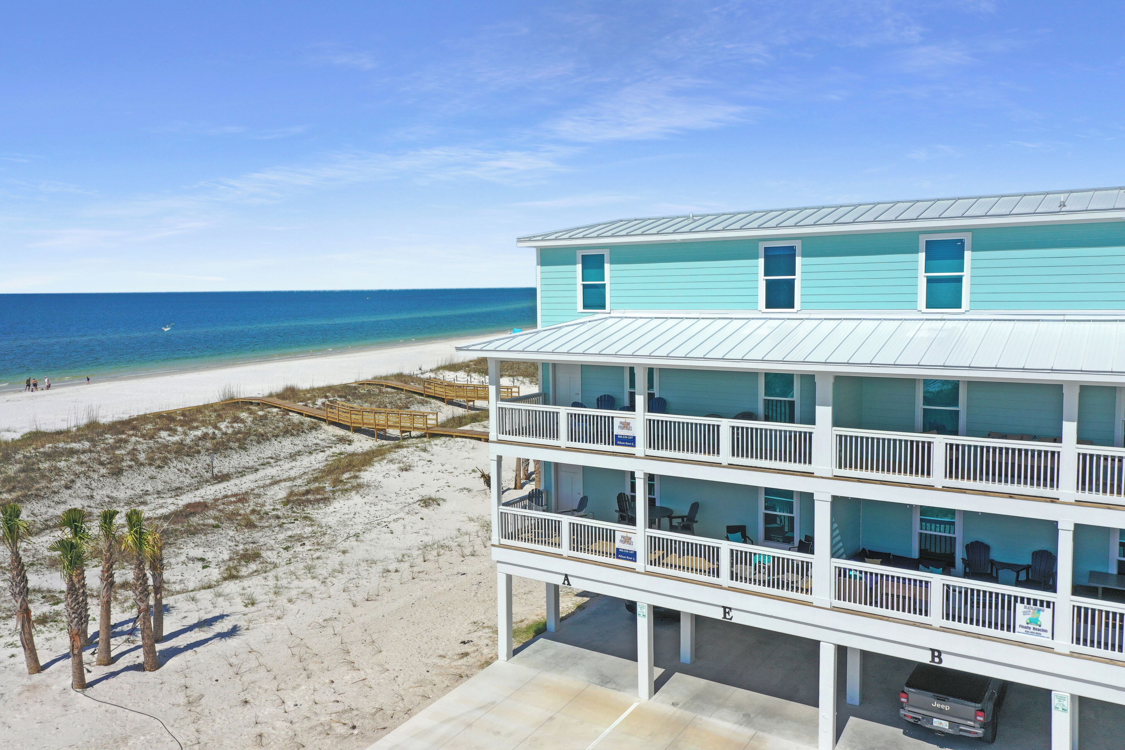A beachfront hotel with multiple balconies, a Jeep parked outside, and a sandy beach area.