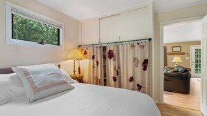 Ein Schlafzimmer mit Bett, Nachttisch, Lampe und Fenster mit Blick auf Bäume.