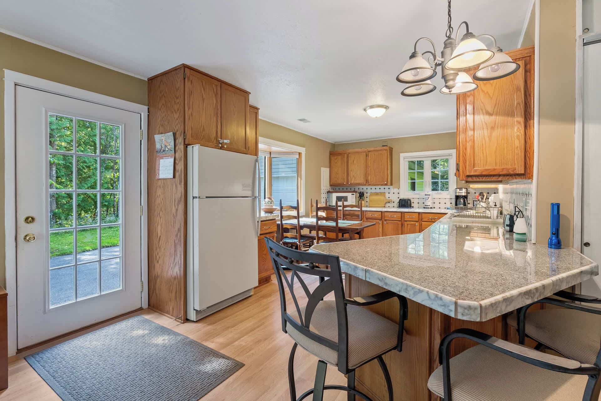 A kitchen with wooden cabinets, a refrigerator, a dining area with chairs, and a large island with a marble countertop.