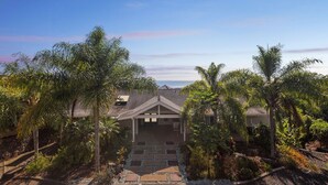 A house with a covered porch, surrounded by palm trees and a stone pathway leading to the entrance. - Pu'ukala Sunset Estate W/ Amazing Ocean Views! 3 Bedroom Home by RedAwning (Kailua-Kona)