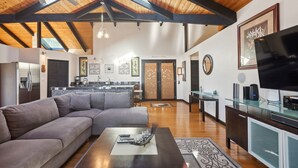 A spacious living area with a large gray sectional sofa, a wooden coffee table, and a glass cabinet with a flat-screen TV. - Pu'ukala Sunset Estate W/ Amazing Ocean Views! 3 Bedroom Home by RedAwning (Kailua-Kona)