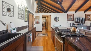 A modern kitchen with a high ceiling, wooden beams, granite countertops, and a gas stove. - Pu'ukala Sunset Estate W/ Amazing Ocean Views! 3 Bedroom Home by RedAwning (Kailua-Kona)