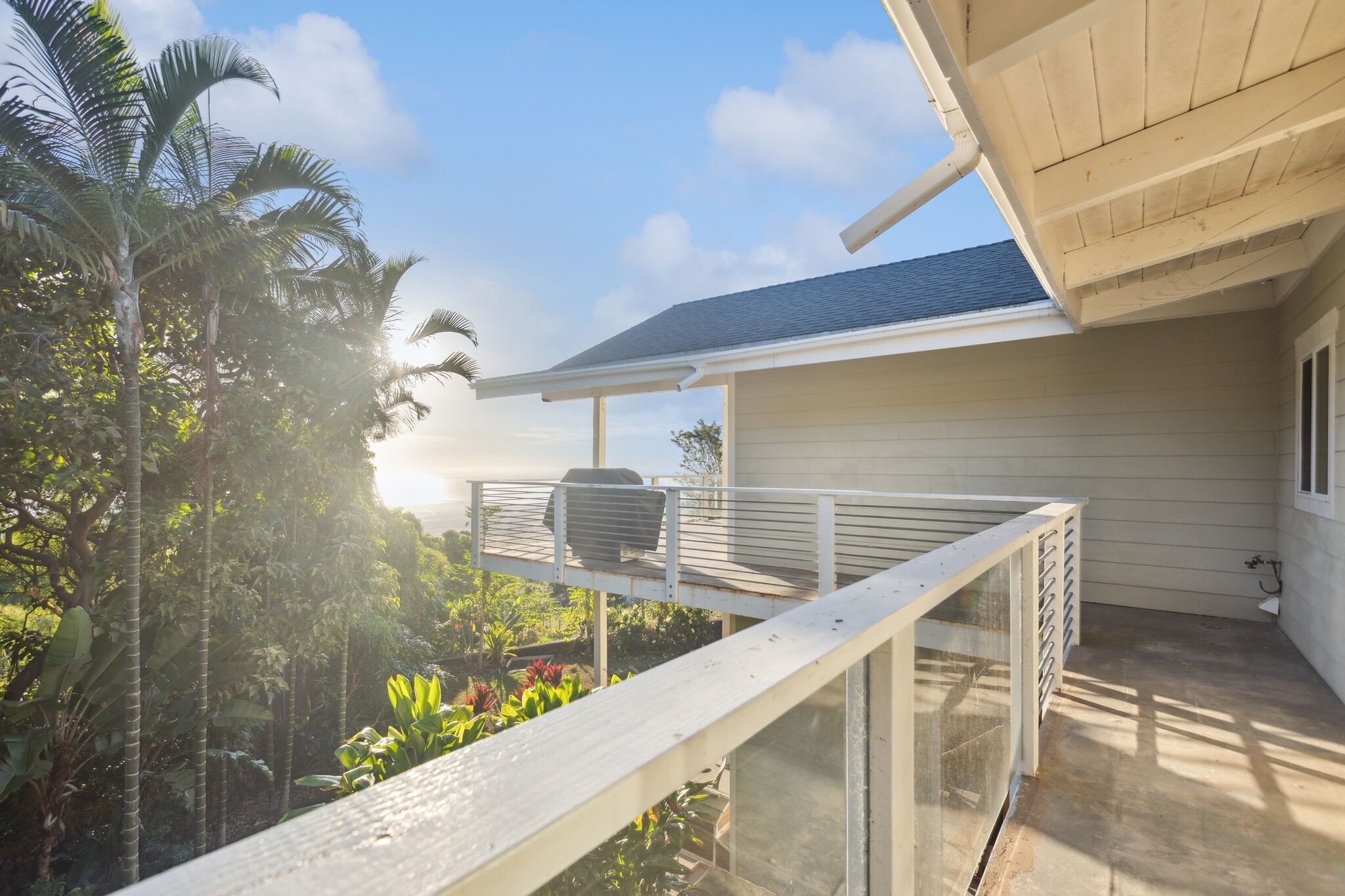 A balcony with a view of tropical vegetation and a building with a white exterior and a dark roof.