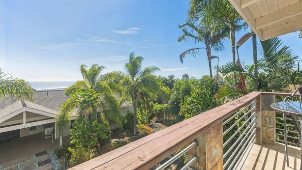 A balcony with a view of a lush garden and a building with a sloped roof. - Charming Pu'ukala Sunset - Near Hiking And Golf 1 Bedroom Home by RedAwning (Kailua-Kona)