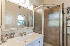 Un baño con tocador blanco, un espejo grande y una cabina de ducha con paredes de vidrio.