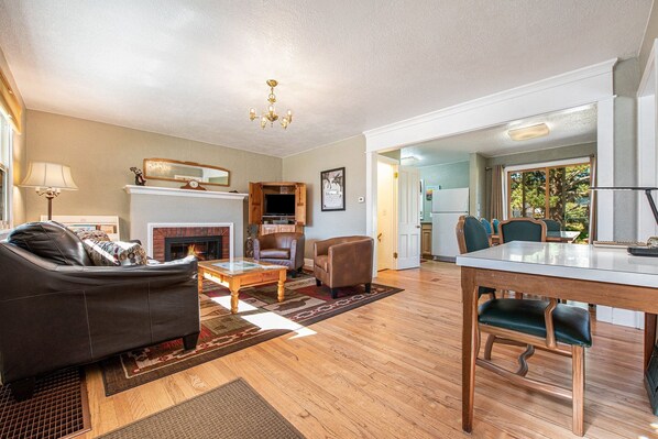 A living room with a fireplace, leather sofa, wooden dining table, and chairs.