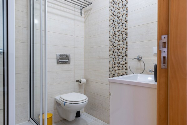Un baño moderno con inodoro, cabina de ducha de vidrio y lavabo con salpicadero de mosaicos.