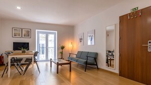 A modern living room with a wooden floor, a sofa, a coffee table, a TV, and a dining area with chairs and a table. - Bombarda 32 (Lisbon)