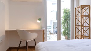 A bedroom with a bed, a desk, a chair, and a window with a view of the outdoors. - Bombarda 32 (Lisbon)
