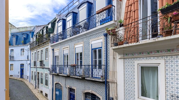 A narrow street with buildings featuring blue and white patterned facades, balconies with metal railings, and a cobblestone street. - Bombarda 32 (Lisbon)