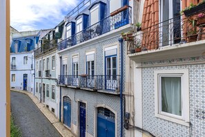 Una estrecha calle flanqueada por edificios con fachadas de patrones azules y blancos, balcones con barandillas metálicas y adoquinado.