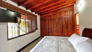Un dormitorio con una cama grande, vigas de madera en el techo, un armario y una ventana con persianas.