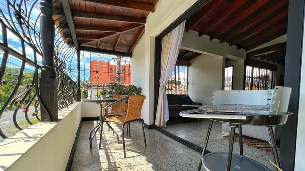 Un balcón con una parrilla, sillas de mimbre y una mesa.