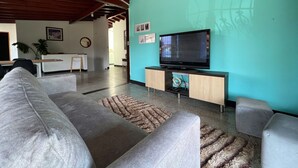 Una sala de estar con un sofá, un reposapiés y un televisor de pantalla plana sobre un mueble de madera.