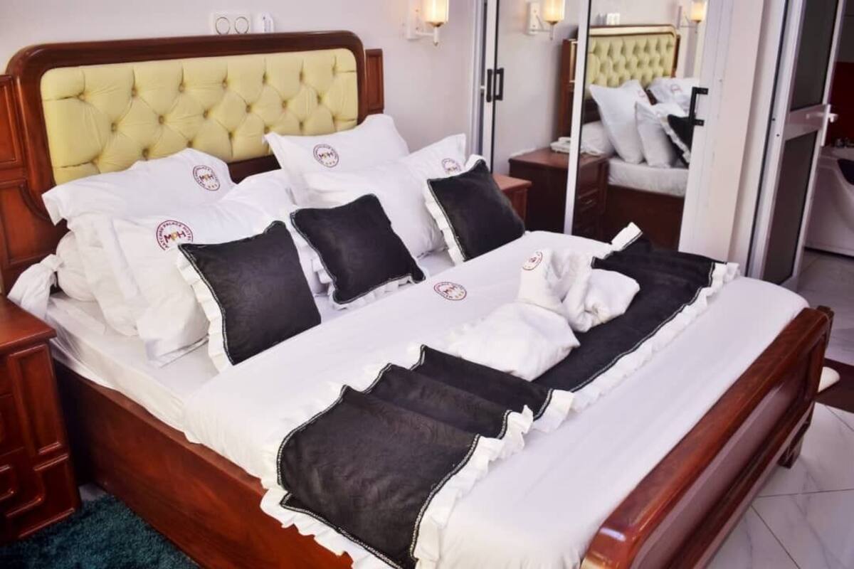 A neatly made bed with white and black bedding, a wooden headboard, and a nightstand with a lamp.