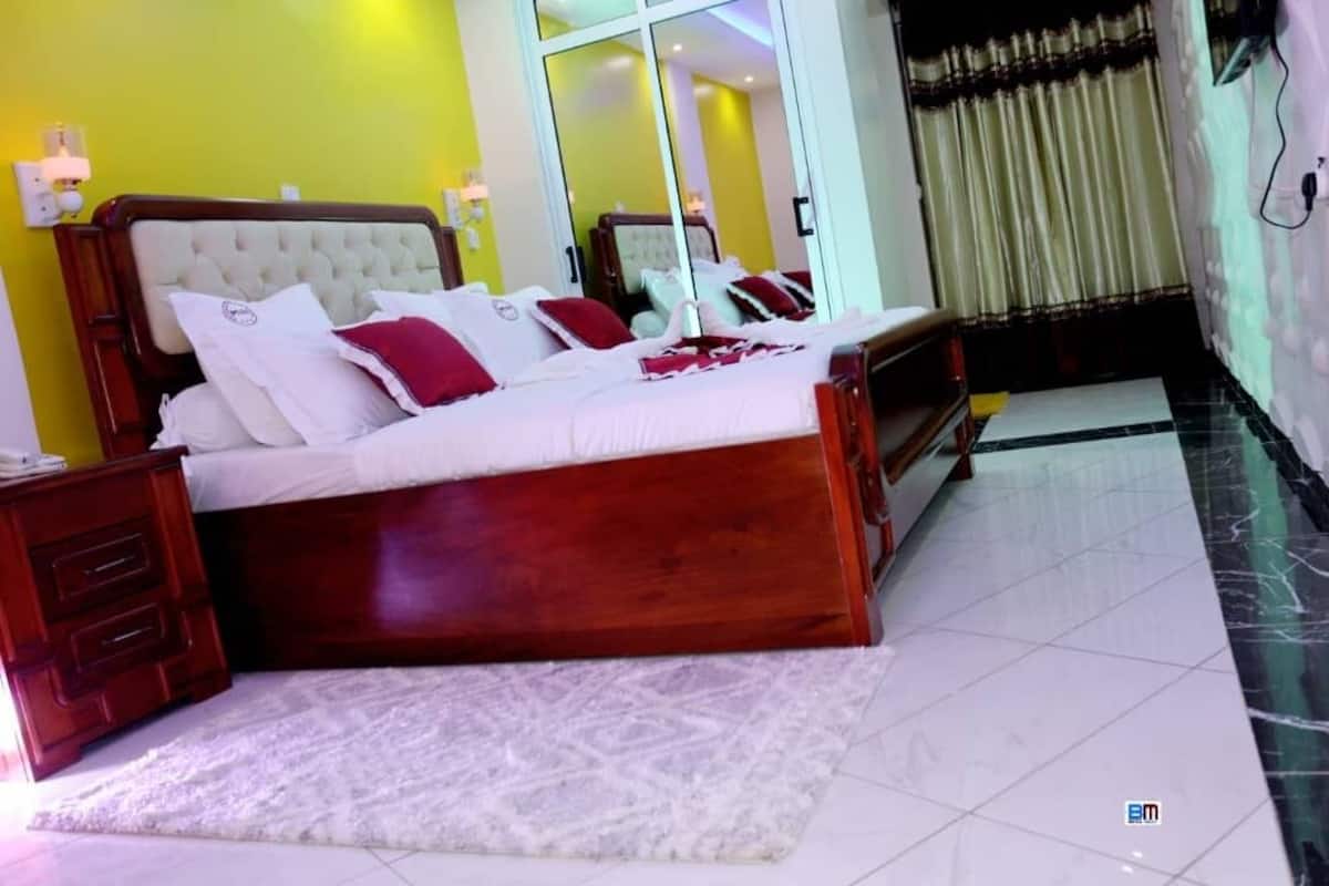 A bedroom with a large bed, a wooden nightstand, a white rug, and a mirror.
