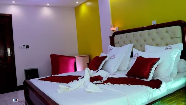 A hotel room with a bed, a nightstand, and a red chair. - MATCHEU PALACE HÔTEL  (Yaoundé)