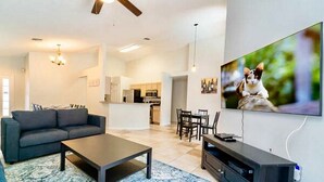 Una sala de estar moderna con un sofá, una mesa de centro y un televisor. Se ve una cocina al fondo.