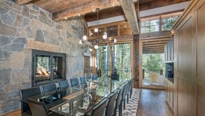 A spacious dining area with a glass table and chairs, a stone fireplace, and a view of the outdoors. - Robber's Roost- Sprawling, Ski In/Out, Arcade, Pool Table, & More! (Mountain Village)