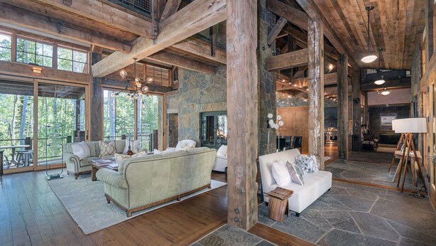 A spacious living area with a large sofa, a smaller sofa, and a coffee table. There are wooden beams and stone walls. - Robber's Roost- Sprawling, Ski In/Out, Arcade, Pool Table, & More! (Mountain Village)
