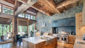 A spacious kitchen with a large island, wooden cabinets, and a stone accent wall. - Robber's Roost- Sprawling, Ski In/Out, Arcade, Pool Table, & More! (Mountain Village)