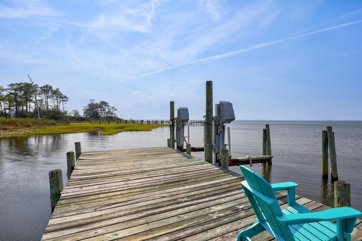 A wooden pier extending into calm water, with a chair and a boat docked at the end.