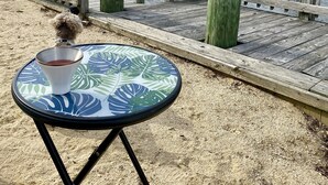 Een houten pier met een tafel en een kop thee, uitkijkend over een rustig wateroppervlak en huizen op de achtergrond.