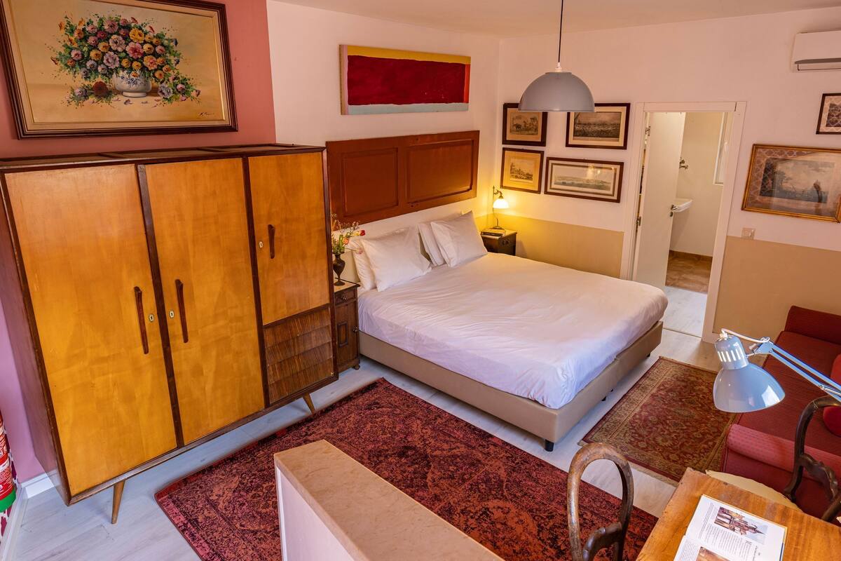 A bedroom with a bed, wooden wardrobe, bedside table, lamp, and a red rug.