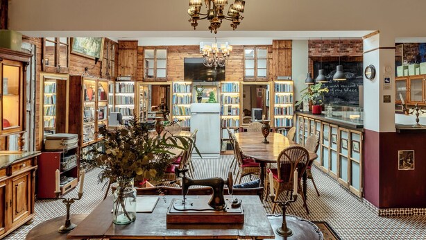 Une bibliothèque chaleureuse avec des étagères en bois, une table centrale entourée de chaises et une machine à coudre ancienne.