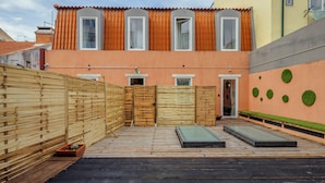 Une cour entourée d’une clôture en bois, un petit jardin et un bâtiment aux murs orange et au toit recouvert de tuiles.