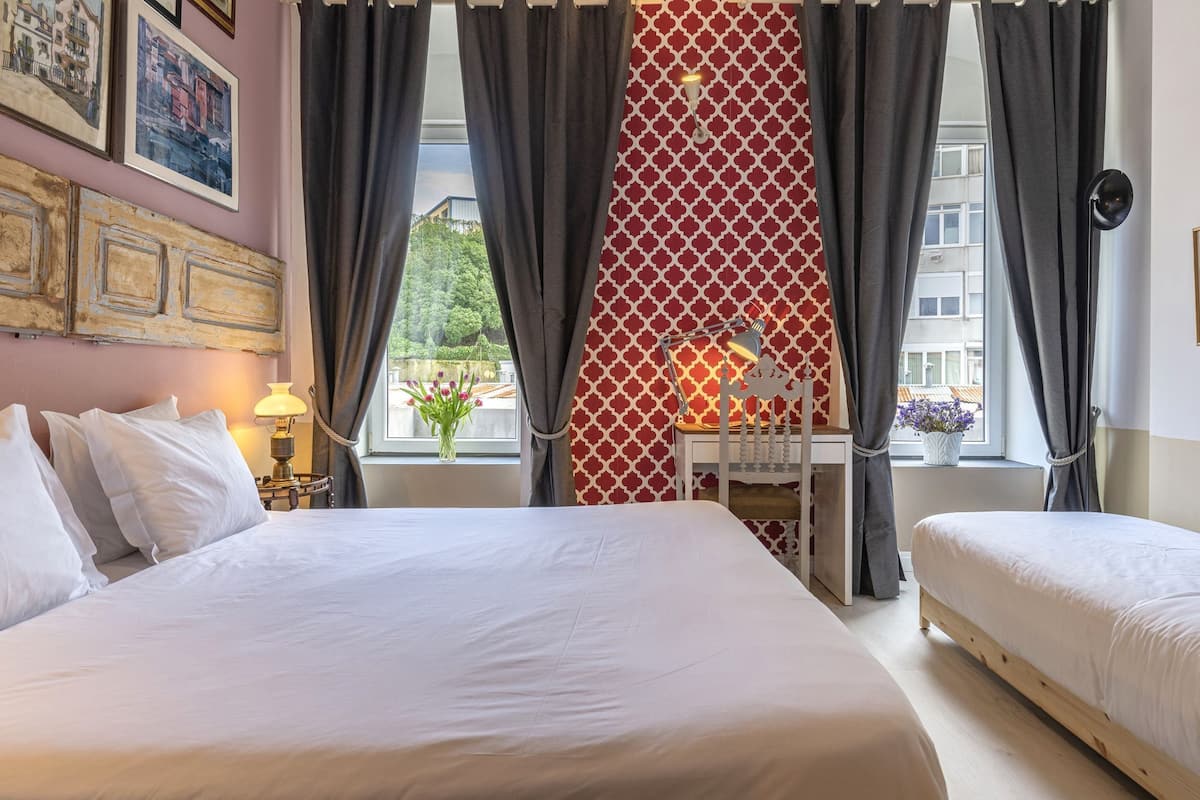 A hotel room with two beds, a desk, and a window with curtains.