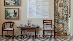Une pièce avec une table en bois, deux chaises, un tableau encadré, une grande affiche informative et une porte rustique.