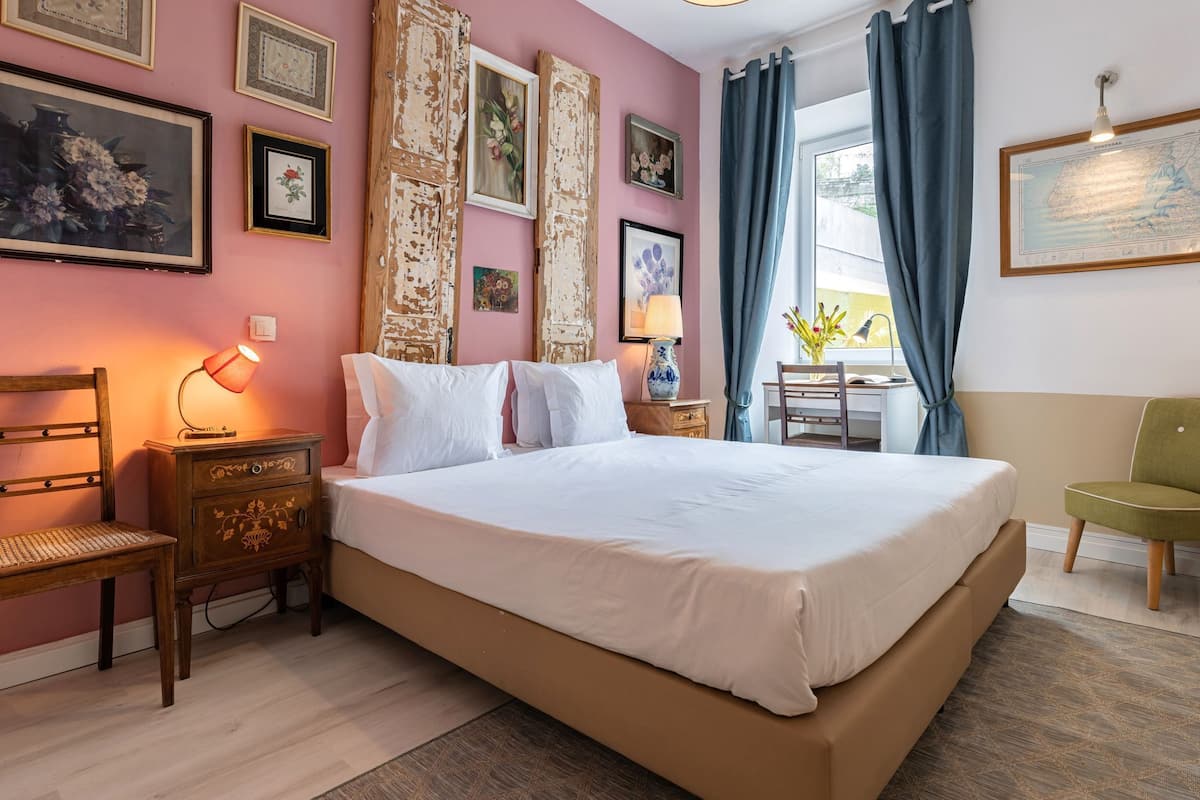 A neatly arranged bedroom with a large bed, a wooden nightstand, a chair, and a desk with a lamp.