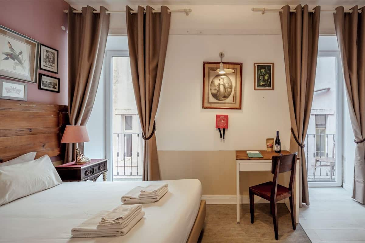 A hotel room with a bed, a desk, a chair, and a window with curtains.