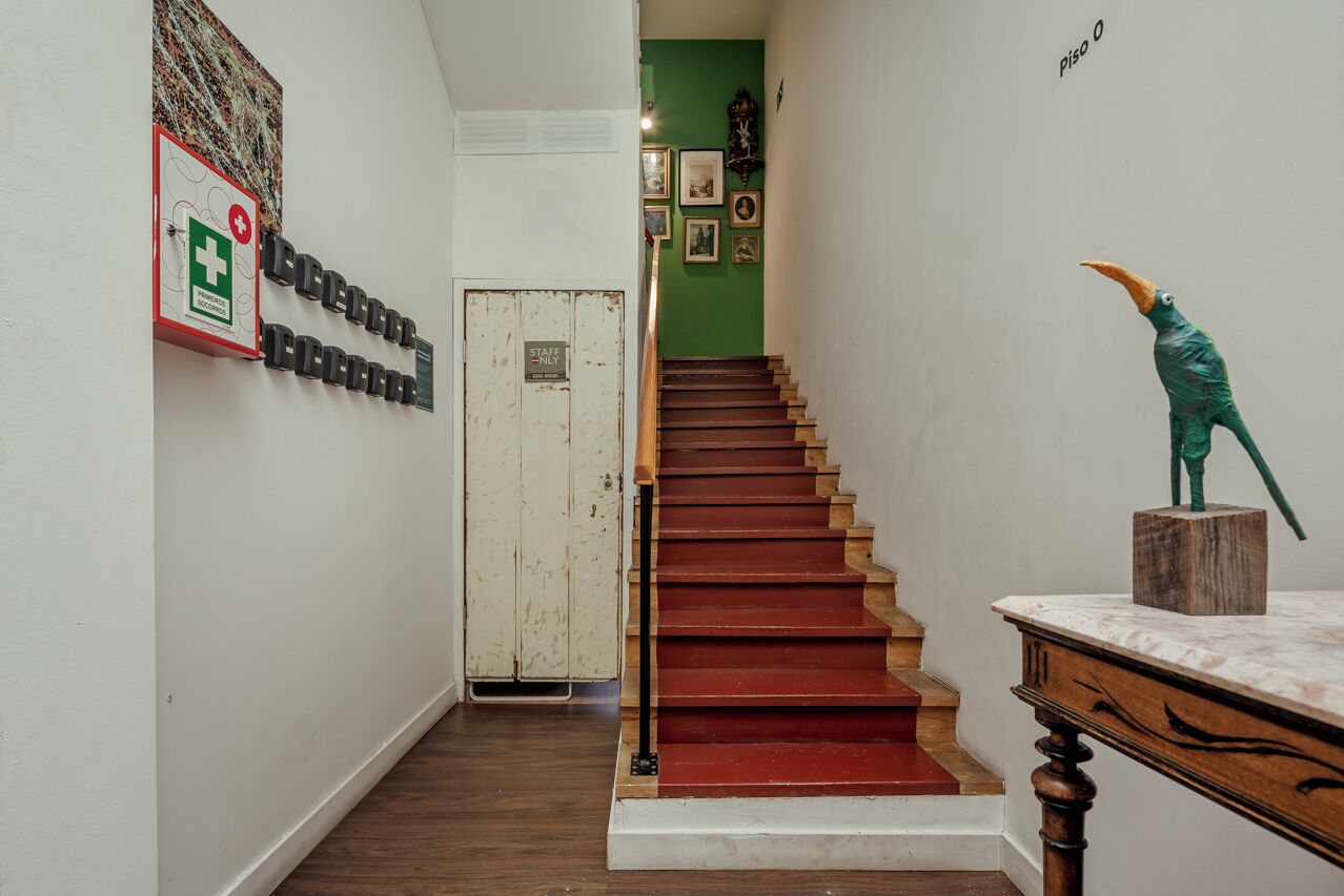 Una escalera con escalones rojos que lleva a una puerta, un cartel de emergencia médica en la pared, y una pared verde con cuadros enmarcados.