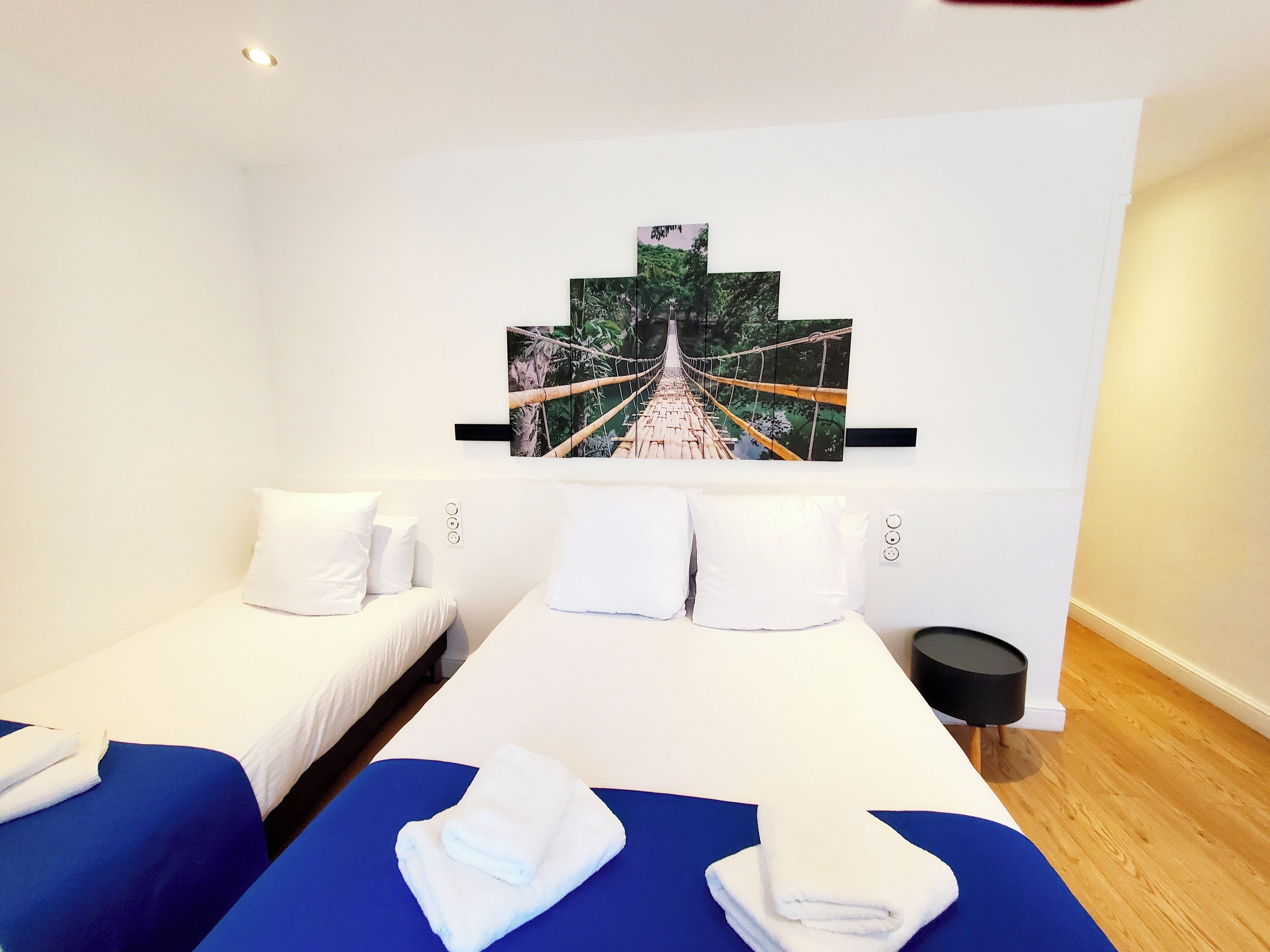 Une chambre d’hôtel avec deux lits, un tableau représentant un pont et une petite table ronde.