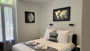 Un dormitorio con una cama grande, dos mesitas de noche, un ventanal con cortinas y dos obras de arte colgadas en la pared.