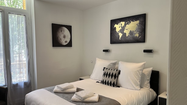 A bedroom with a large bed, two bedside tables, a window with curtains, and two wall-mounted artworks.