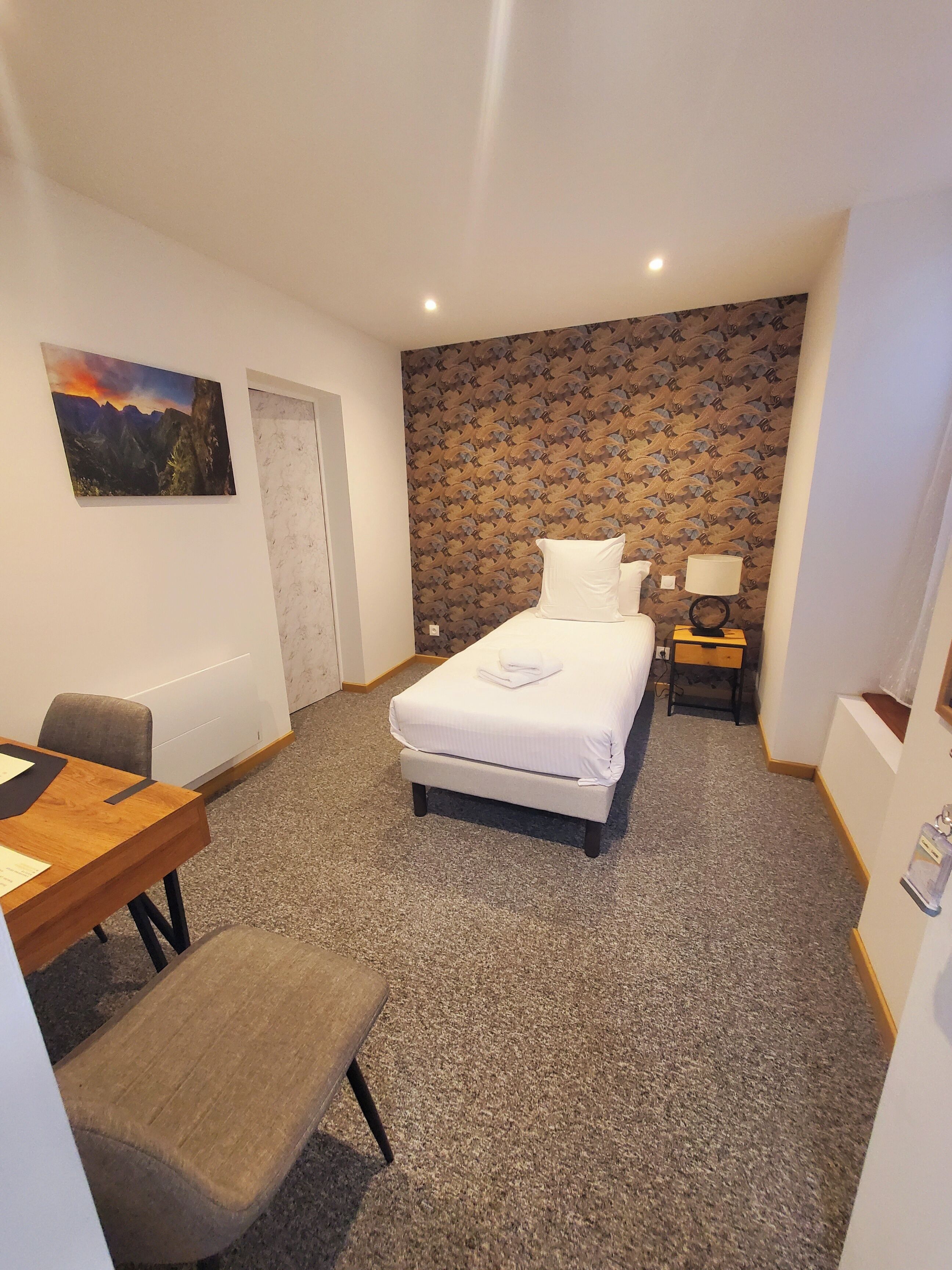 Une chambre d’hôtel comprenant un lit, un bureau, une chaise, une table de chevet et une lampe.