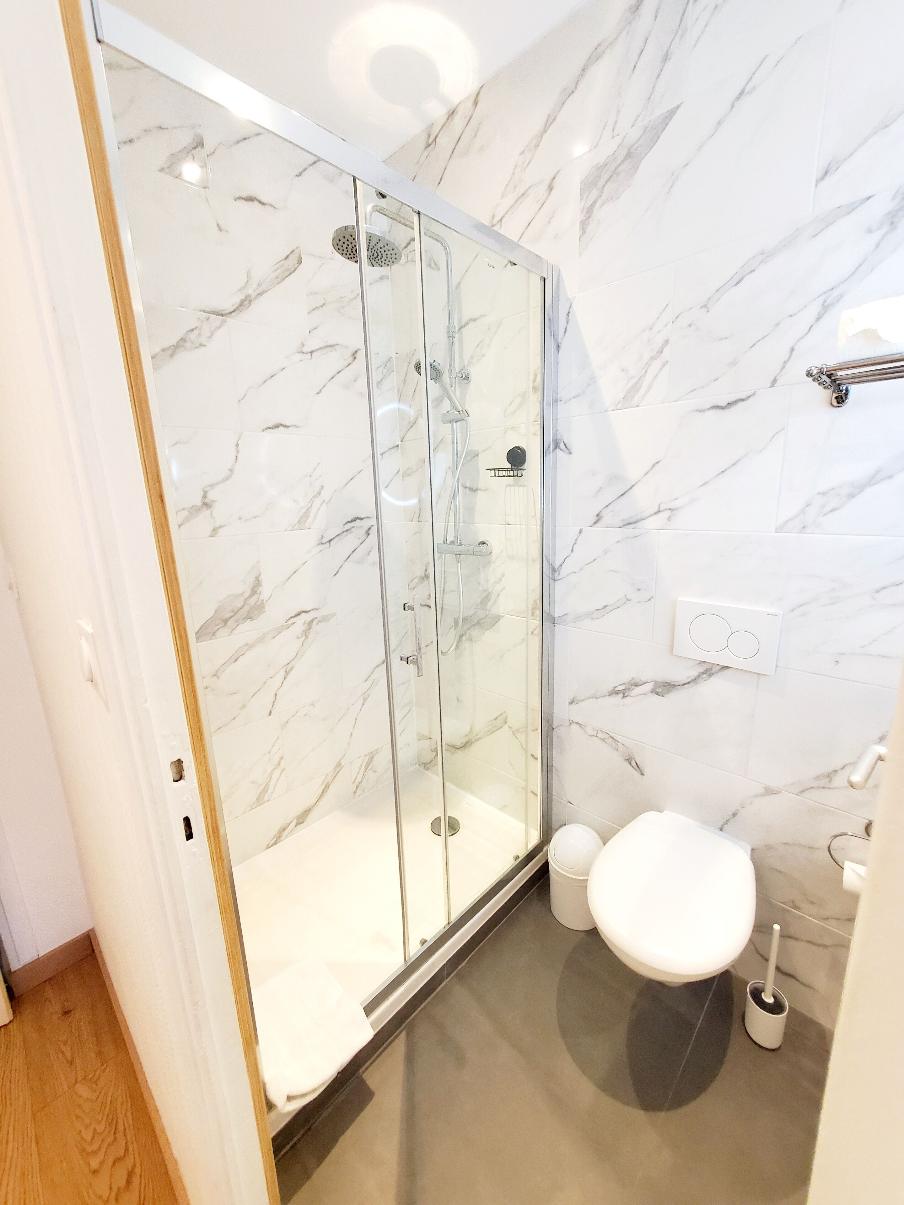 Un baño moderno con ducha envuelta en vidrio, inodoro y paredes con diseño de mármol.