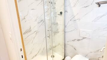 Un baño moderno con ducha envuelta en vidrio, inodoro y paredes con diseño de mármol.