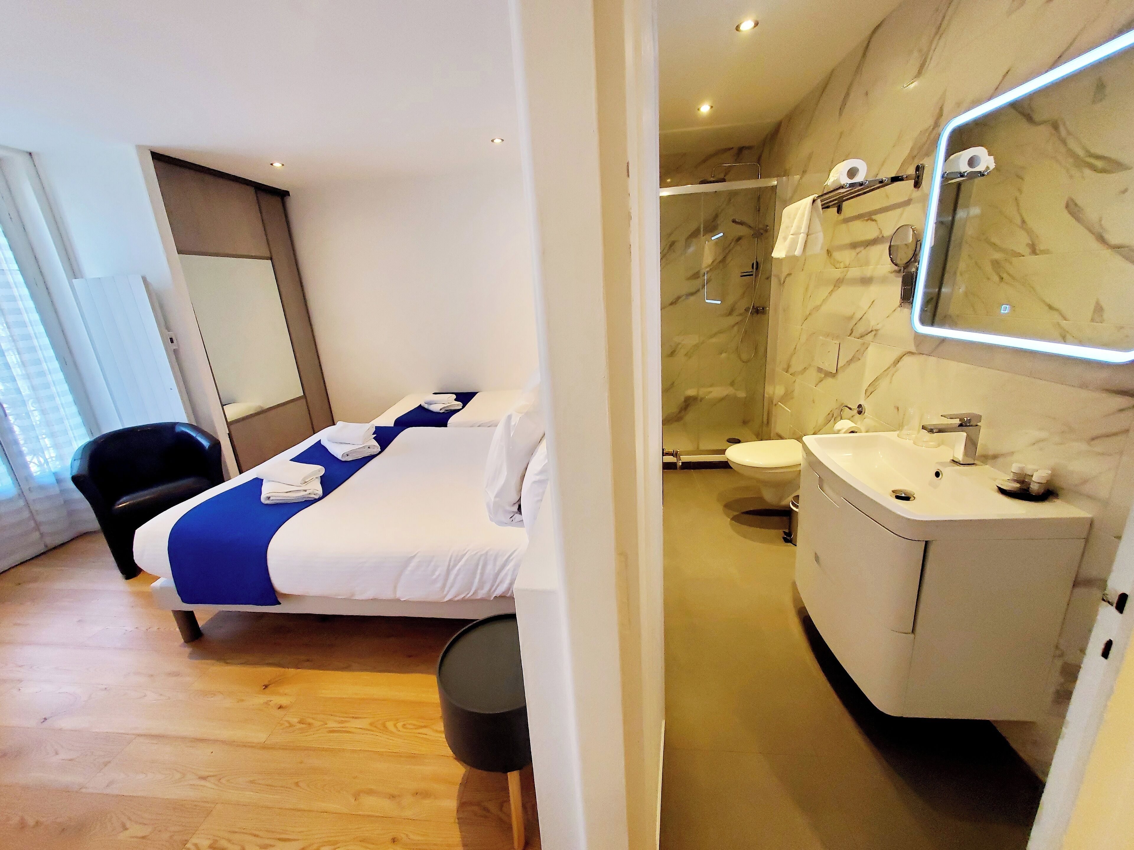 A hotel room with a bed, a bathroom with a sink and mirror, and a shower.