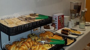 A buffet with various breads and pastries, a decorative wall piece, and breakfast items like cereal and milk.